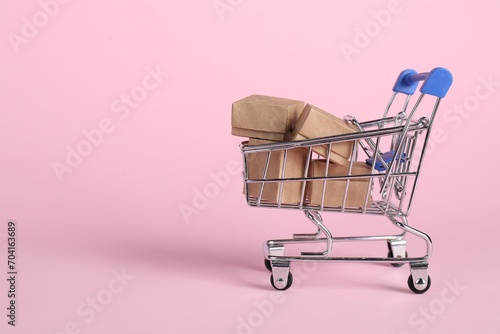 Small metal shopping cart with cardboard boxes on pink background, space for text