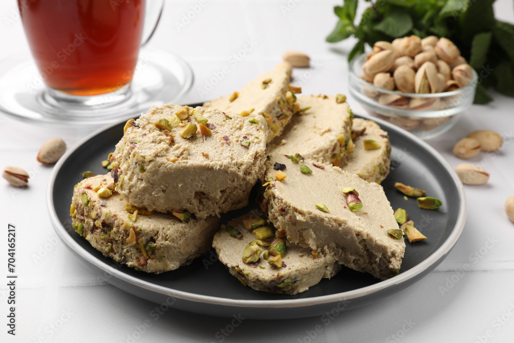 Tasty halva with pistachios served on white tiled table, closeup
