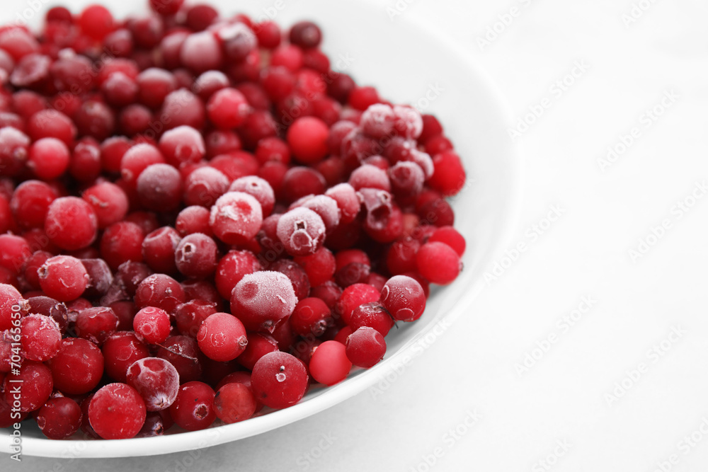 Frozen red cranberries in bowl on white table, closeup Frozen red cranberries in bowl on white table, closeup