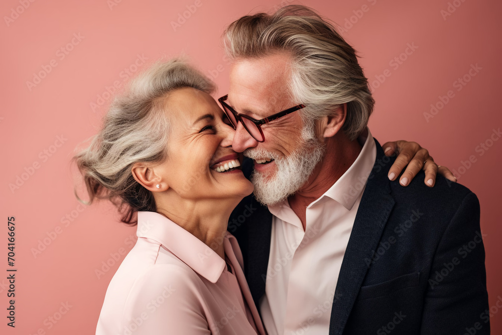 Elegant elderly couple hugging, looking at each other, laughing, pink background Elegant elderly couple hugging, looking at each other, laughing, pink background