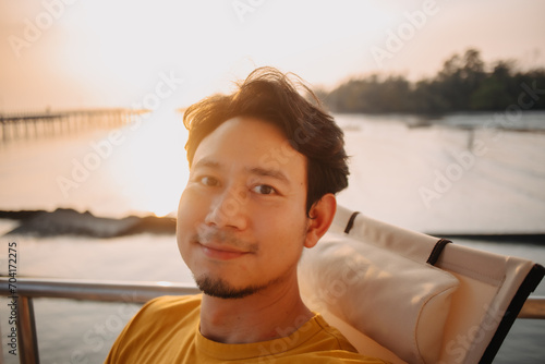 Portrait of happy smile Asian man selfie himself sits and relax for holiday trip in the resort with sunset sea view.