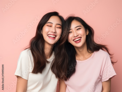 Asian sisters laughing happily isolated on pink background, happy family concept