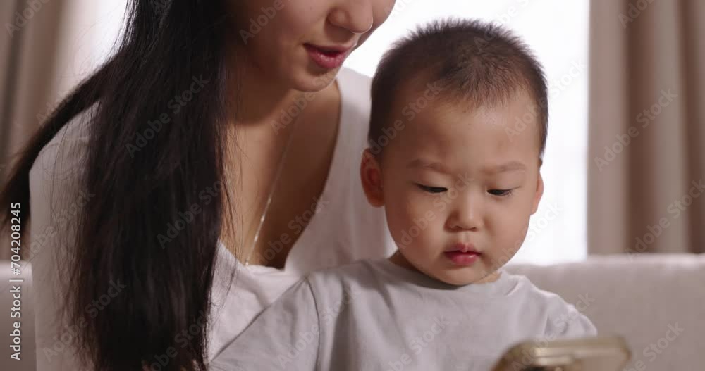 Asian mom and toddler spending time together. Multiethnic asian woman mother boy son toddler watching videos on internet online from smartphone watching cartoons. Interested kid, happy smiling mom. Asian mom and toddler spending time together. Multiethnic asian woman mother boy son toddler watching videos on internet online from smartphone watching cartoons. Interested kid, happy smiling mom.