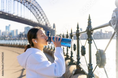 Asian woman in sportswear drinking water from a bottle after jogging exercise in the morning. Healthy girl athlete enjoy urban outdoor lifestyle do sport training running fitness workout in the city.