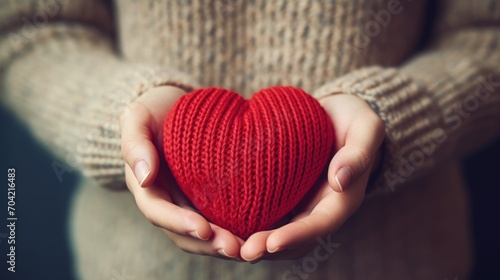 Close-up of a woman in a warm sweater holding a knitted red heart in her hands. Valentine's Day greeting card. A symbol of love. photo