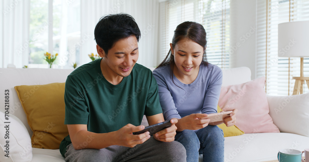 Fototapeta premium Young adult asia cute sweet couple enjoy playing sport match game online in esport race lover at home sofa couch. Two Gen Z people man and woman gamer happy relax smile laugh joy fun video gaming app.