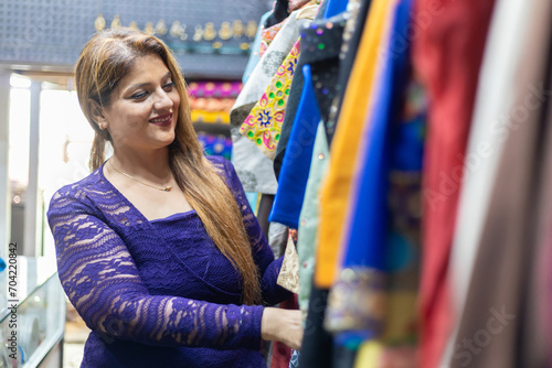 Portrait of happy indian woman shopping in clothing store, choosing stylish clothes in mall. shopping people, sale, fashion concept.