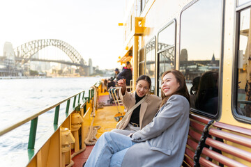 Happy Asian woman friends sitting on ferry boat crossing Sydney harbour in Australia. Attractive girl enjoy and fun urban outdoor lifestyle shopping and travel in the city on holiday vacation.
