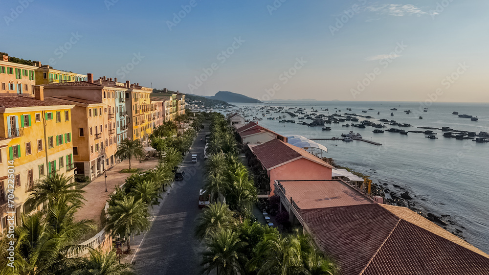 A tranquil coastal streetscape at twilight with palm-lined promenade, colorful buildings, and a bay speckled with boats, suggesting a serene vacation destination