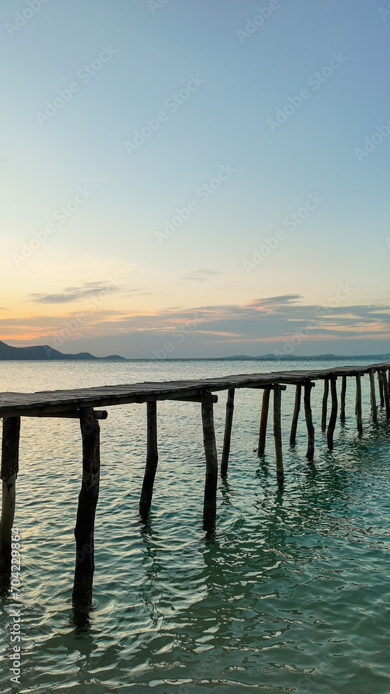 An old wooden pier stretches into calm sea waters with a tranquil sunset over the horizon, conveying a serene and peaceful concept