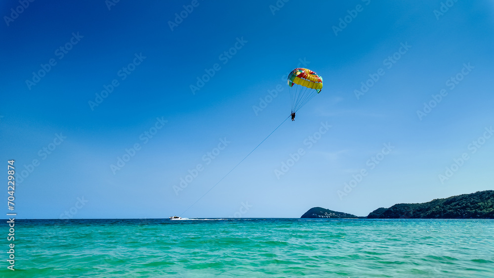 A person parasailing over a calm sea with a speedboat and tropical hills in the background, depicting adventure and vacation concepts A person parasailing over a calm sea with a speedboat and tropical hills in the background, depicting adventure and vacation concepts