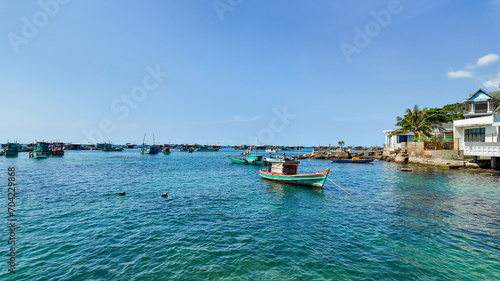 A tranquil seaside scene with boats moored in a clear blue bay adjacent to a coastal village under a vast sky, conveying a sense of summer serenity © fotoworld