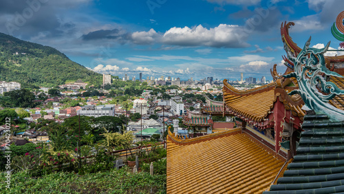 The roof of a Chinese Kek Lok Si Temple against the urban landscape. Rows of lamps along the curved edges, elegant decorative curls. City houses, skyscrapers among the green vegetation. Malaysia. 