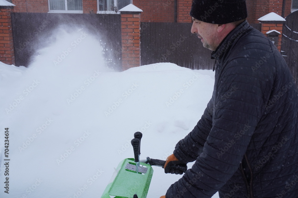 A man cleans snow in the winter in the courtyard of the house,  man cleaning snow with a snow blower