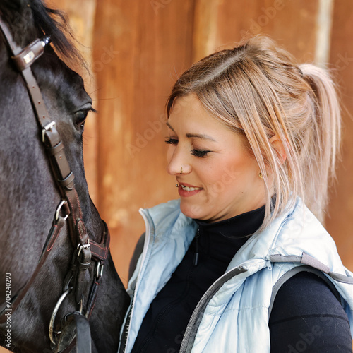 Girl blonde in blue quilted vest with ponytail plays with her horse, portraits of the woman with focus on her head close-up.