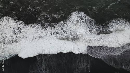 Cinematic aerial top view over ocean waves crashing on Iceland Solheimasandur black sand beach photo