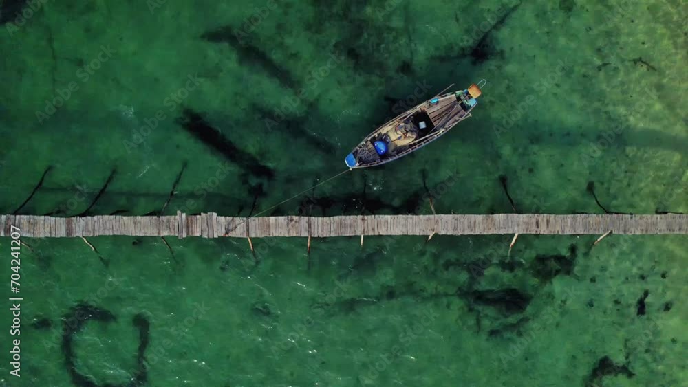 Aerial view of a solitary boat next to a wooden pier on a clear green-water sea, illustrating serene nature or tranquil travel concepts Aerial view of a solitary boat next to a wooden pier on a clear green-water sea, illustrating serene nature or tranquil travel concepts