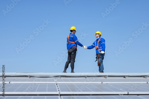 Engineers with handshake gesture on solar panels against blue sky