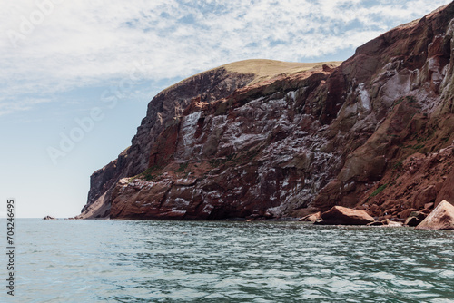vue sur une falaise en roche rouge avec des fientes d'oiseau en bord de mer avec du gazon sur le dessus lors d'une journée ensoleillée