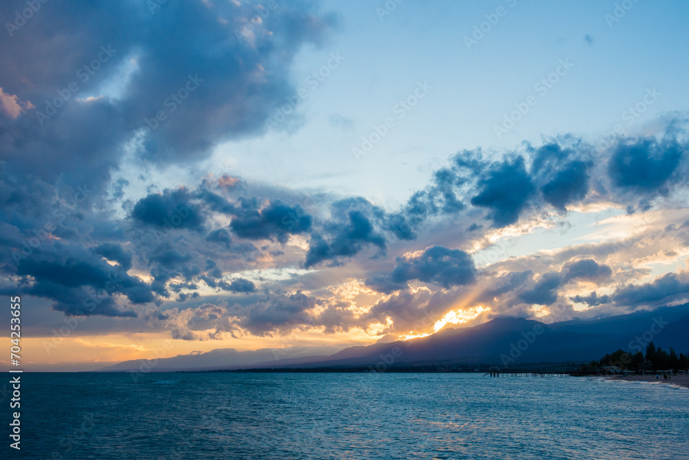 Fototapeta premium Colorful sunset on the sea. Mountain lake in the rays of the orange sun. Kyrgyzstan, Lake Issyk-Kul. natural background