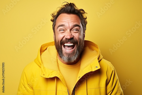 Excited smiling happy laughinh adult man with beard in rain coat on isolated yellow background studio portrait. Positive people anouncement concept. Empty space place for text copy paste © Valeriia