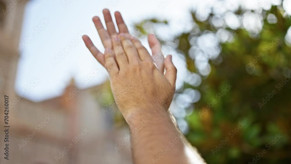 Hispanic young adult man clapping hands outdoors in nature with blurred green foliage and buildings background. Hispanic young adult man clapping hands outdoors in nature with blurred green foliage and buildings background.