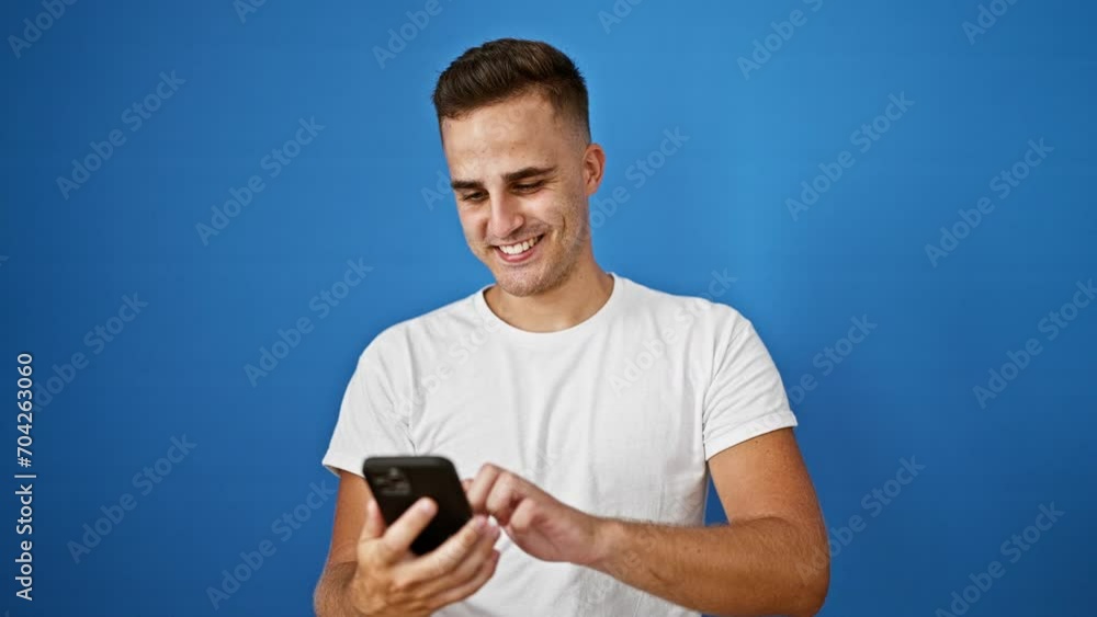 Smiling young hispanic man using smartphone against isolated blue wall Smiling young hispanic man using smartphone against isolated blue wall