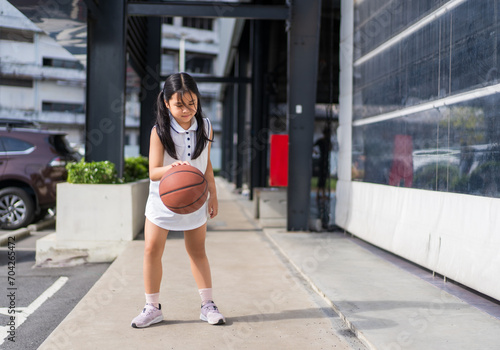 asian child or kid girl fun playing basketball and smile training to learning bouncing and raising ball alone at sports stadium school or basketball court for exercise on sport day and holiday photo