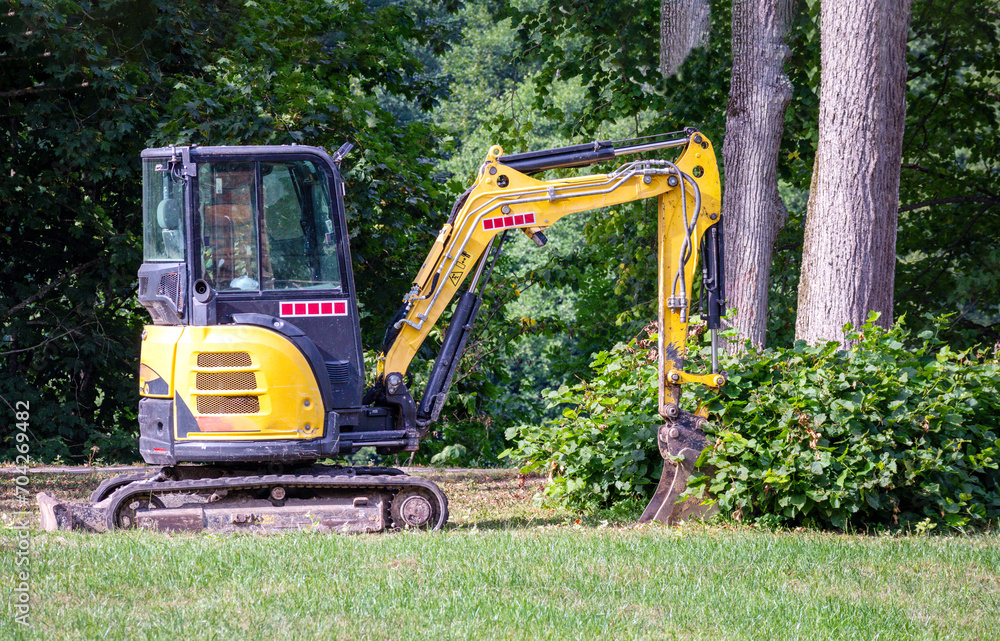 A small yellow tractor with a bucket and tracks in the park near a tree A small yellow tractor with a bucket and tracks in the park near a tree