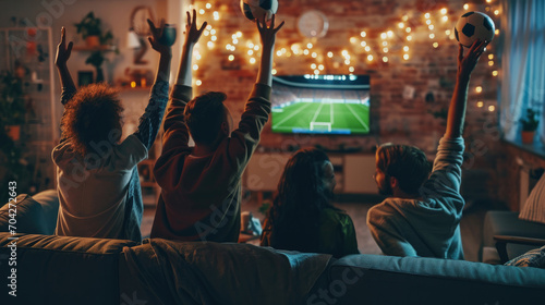 Back view group of young friends watching football match from television at home. Young people cheering sport tournament live broadcast together. photo