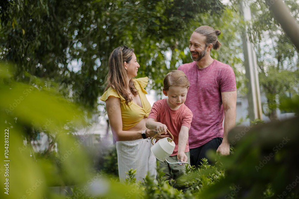 Fototapeta premium Caucasian family with little kids son planting and taking care plants together in house backyard outdoors. Smiling Father, Mother and Son having fun at garden home. Happy family time concept.