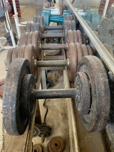 Old and new dumbbell weights lined up on a rack at a rustic home gym