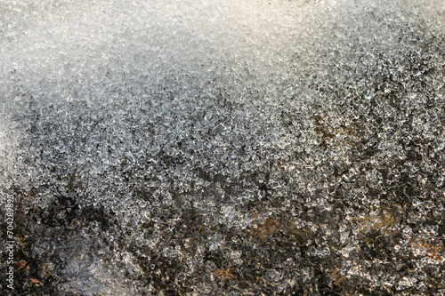 Macro shot of melting snow on black asphalt on a sunny spring day