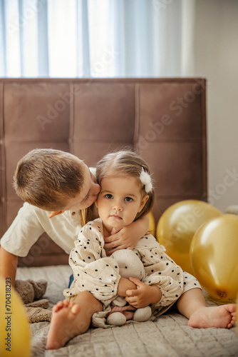 Принти на полотні Big brother is kissing his little sister while sitting surrounded by balloons