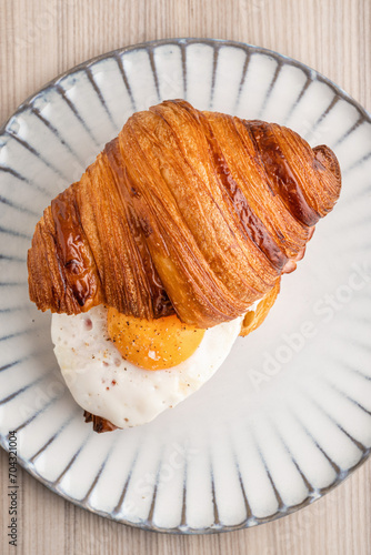 Croissant with fried egg and pastrami on a gray plate, top view