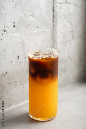 Coffee drink with orange juice in a beautiful thin glass, against the background of a concrete wall