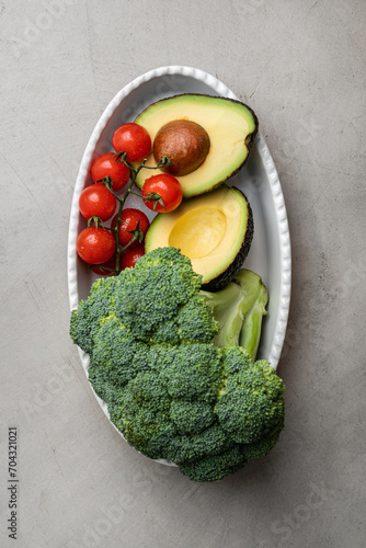 Fresh broccoli, cherry tomatoes and avacado halves on a white plate. Comfort food concept