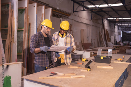 Young affrican american and white men carpenter labor, craftman working in wood workshop together. Looking paper Timber industry and furniture industry.