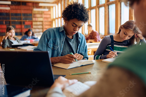 Black high school student learning with friends in library.