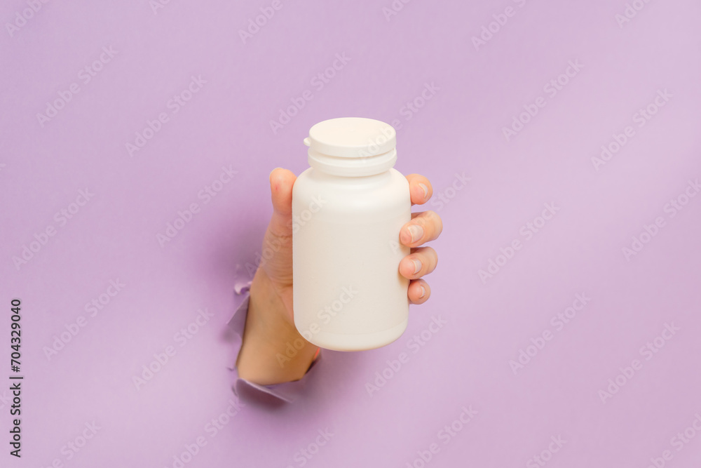 View on white bottle plastic tube in hands on lilac background. Packaging for pills, capsules, supplements. Cosmetics View on white bottle plastic tube in hands on lilac background. Packaging for pills, capsules, supplements. Cosmetics