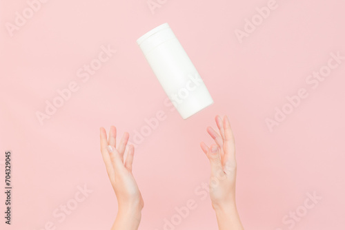 Shampoo, hair conditioner or body lotion bottle in hands in pink background. Cosmetics bottle