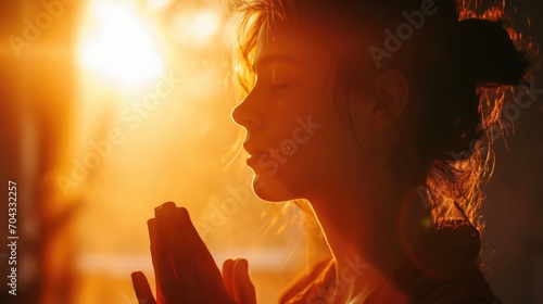 Young woman praying on the background of the setting sun.