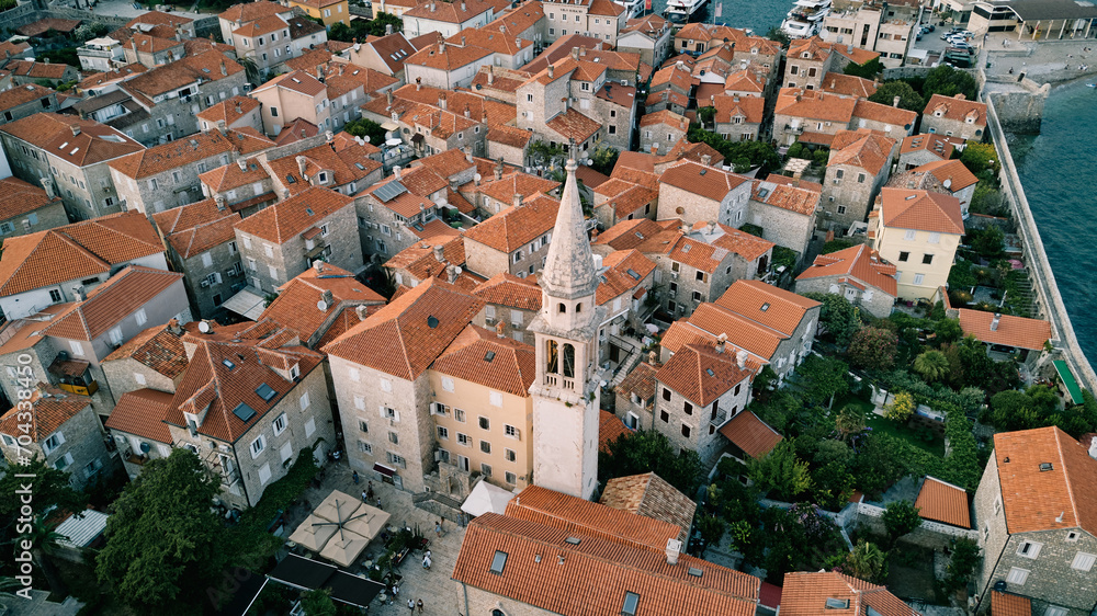 High bell tower of the Church of St. Ivan among the ancient houses of Budva. Montenegro. Drone