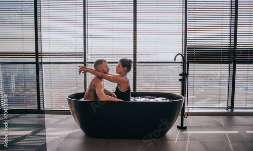 Couple in bathtub, intimate moment with cityscape background, modern luxury.
