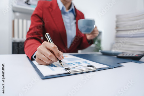 individual in a red blazer, analyzing a bar graph on a clipboard while holding a coffee mug, indicative of working on yearly tax documents. photo