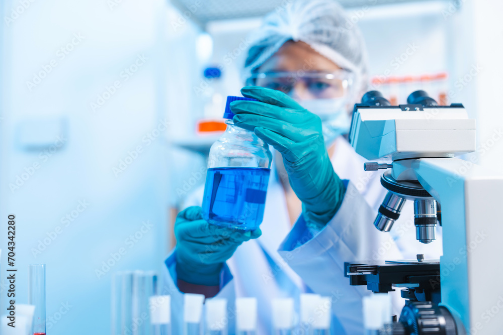 Asian people scientist in lab coat and protective gloves working with test tubes with green and red liquids, with microscope and other test tubes in the background in laboratory. Asian people scientist in lab coat and protective gloves working with test tubes with green and red liquids, with microscope and other test tubes in the background in laboratory.