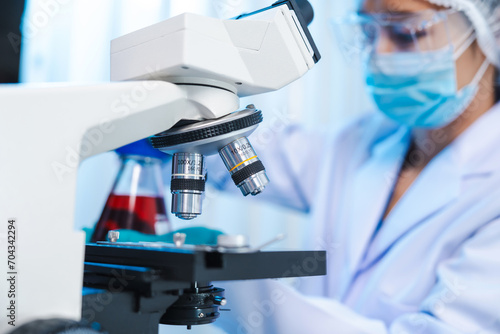 Fotografía Asian people scientist in lab coat and protective gloves working with test tubes with green and red liquids, with microscope and other test tubes in the background in laboratory