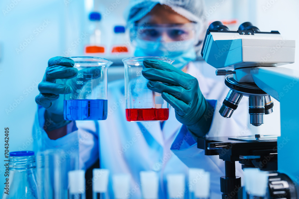 Asian people scientist in lab coat and protective gloves working with test tubes with green and red liquids, with microscope and other test tubes in the background in laboratory. Asian people scientist in lab coat and protective gloves working with test tubes with green and red liquids, with microscope and other test tubes in the background in laboratory.