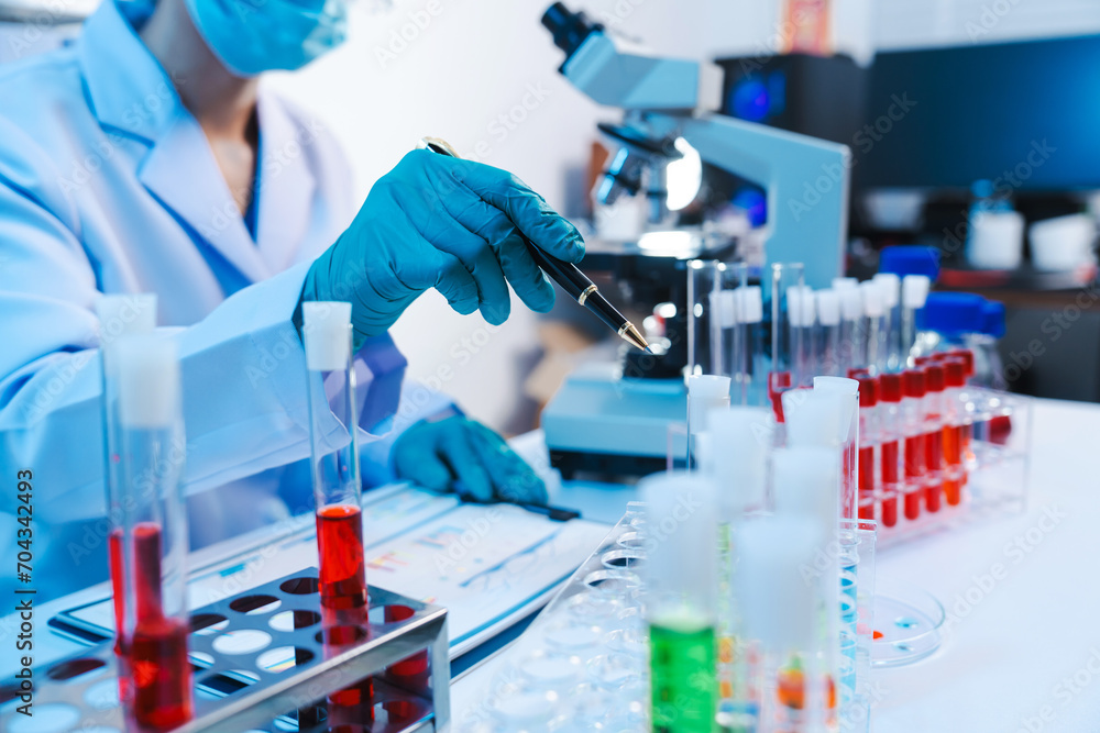 Asian people scientist in lab coat and protective gloves working with test tubes with green and red liquids, with microscope and other test tubes in the background in laboratory. Asian people scientist in lab coat and protective gloves working with test tubes with green and red liquids, with microscope and other test tubes in the background in laboratory.