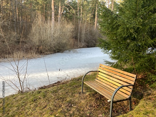 empty bench in spring evening near small lake with melting ice
